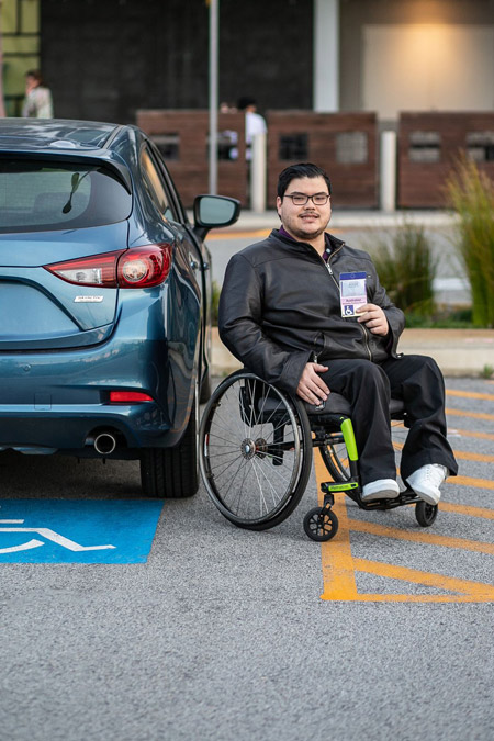 Young man in wheelchair holding up his ACROD parking permit