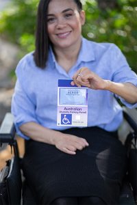 Young woman in a wheelchair holding up An ACROD Disability Parking Permit